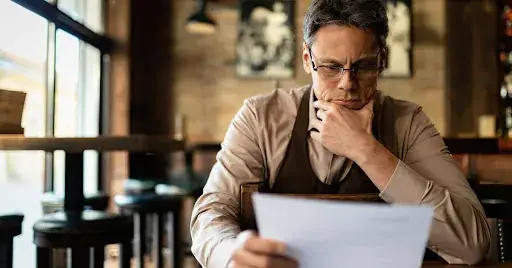 Businessman reviewing documents in a café, representing efficient BPO services and strategic outsourcing solutions for small business.